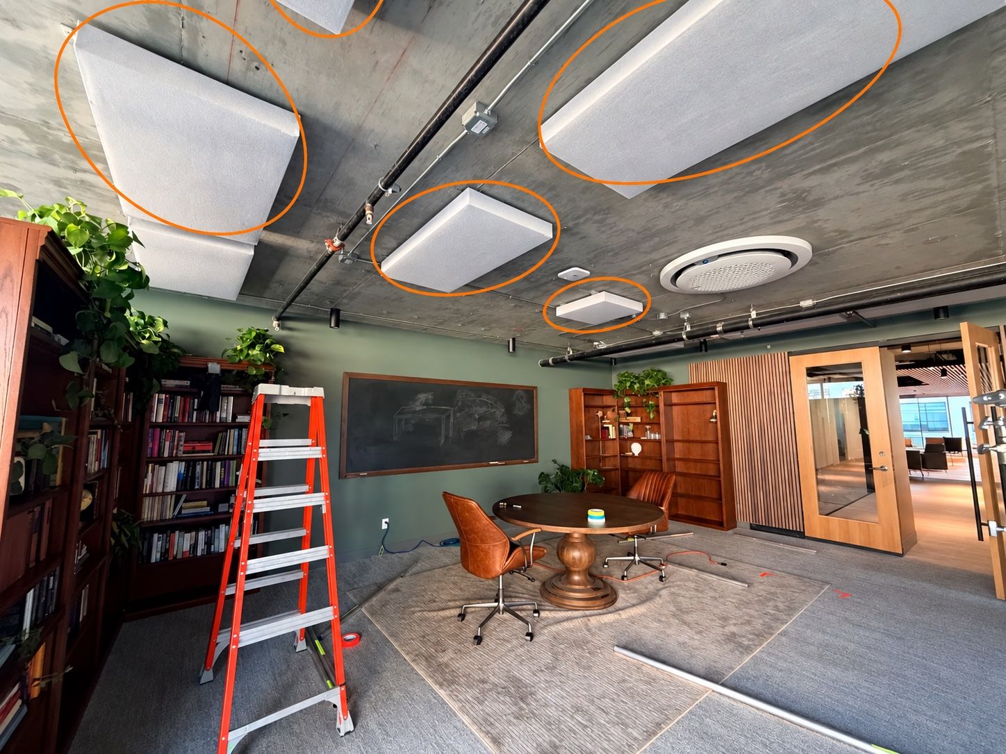 Acoustic panels circled on the concrete ceiling of a library room, with a ladder and a round table below