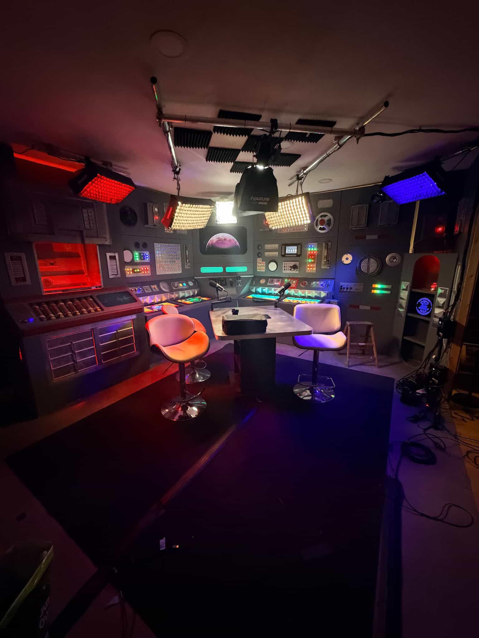 The finished retro mission control set, lit in red and blue, with two chairs at the console