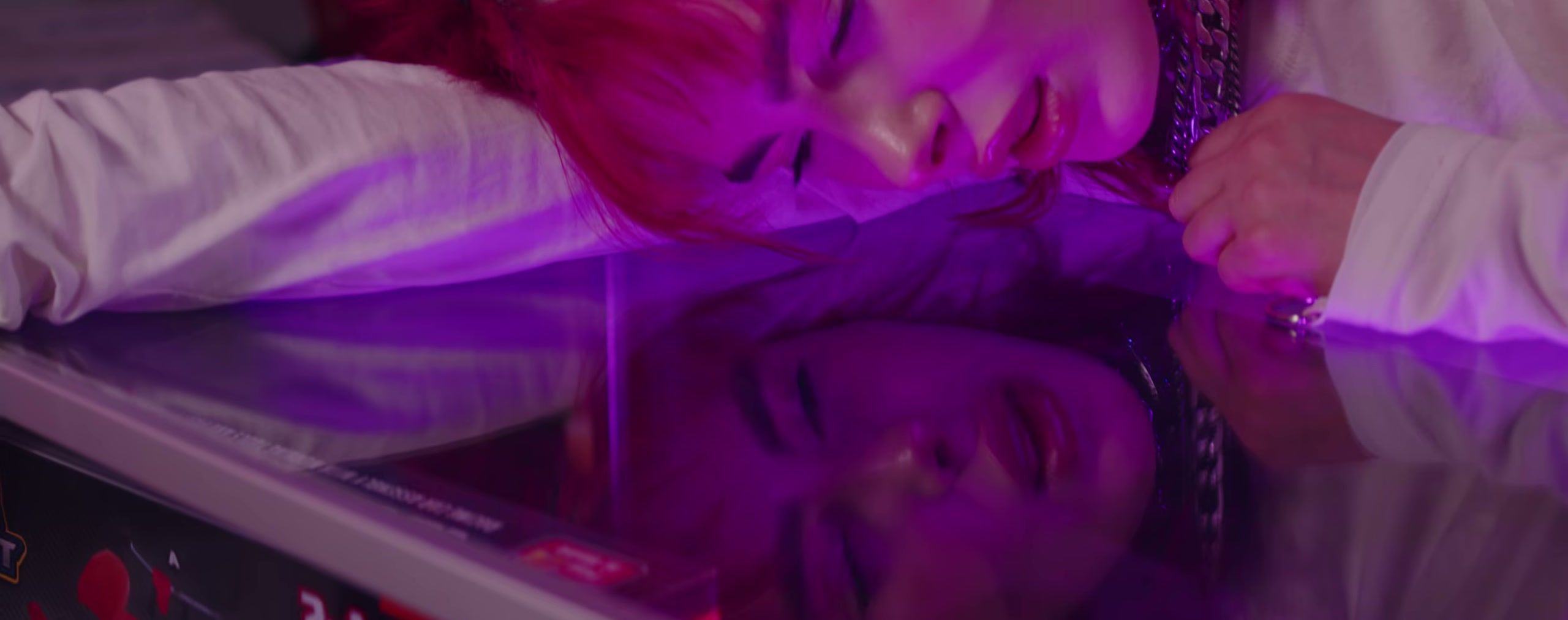 A performer in pink light lies with their face reflected on a glossy surface.