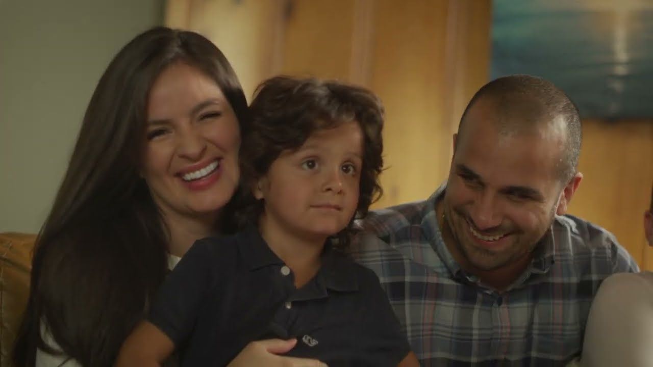 A laughing mother holds her curly-haired son on the sofa while the father smiles beside them