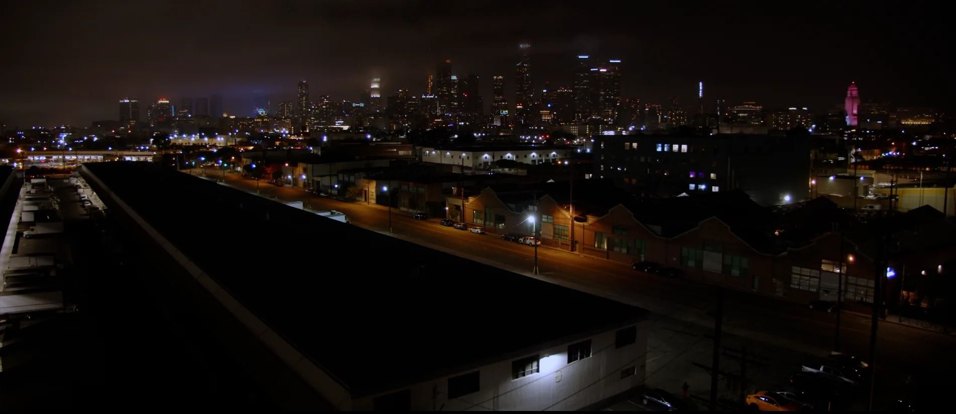 The downtown Los Angeles skyline at night over the rooftops of the warehouse district.