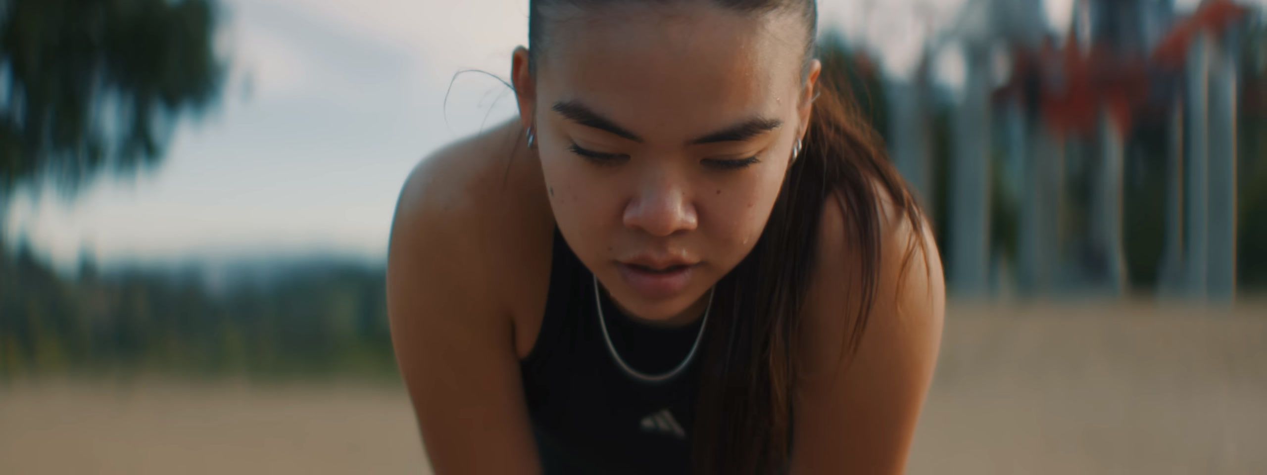 Out of breath, a young woman bends forward with her hands on her knees outdoors.