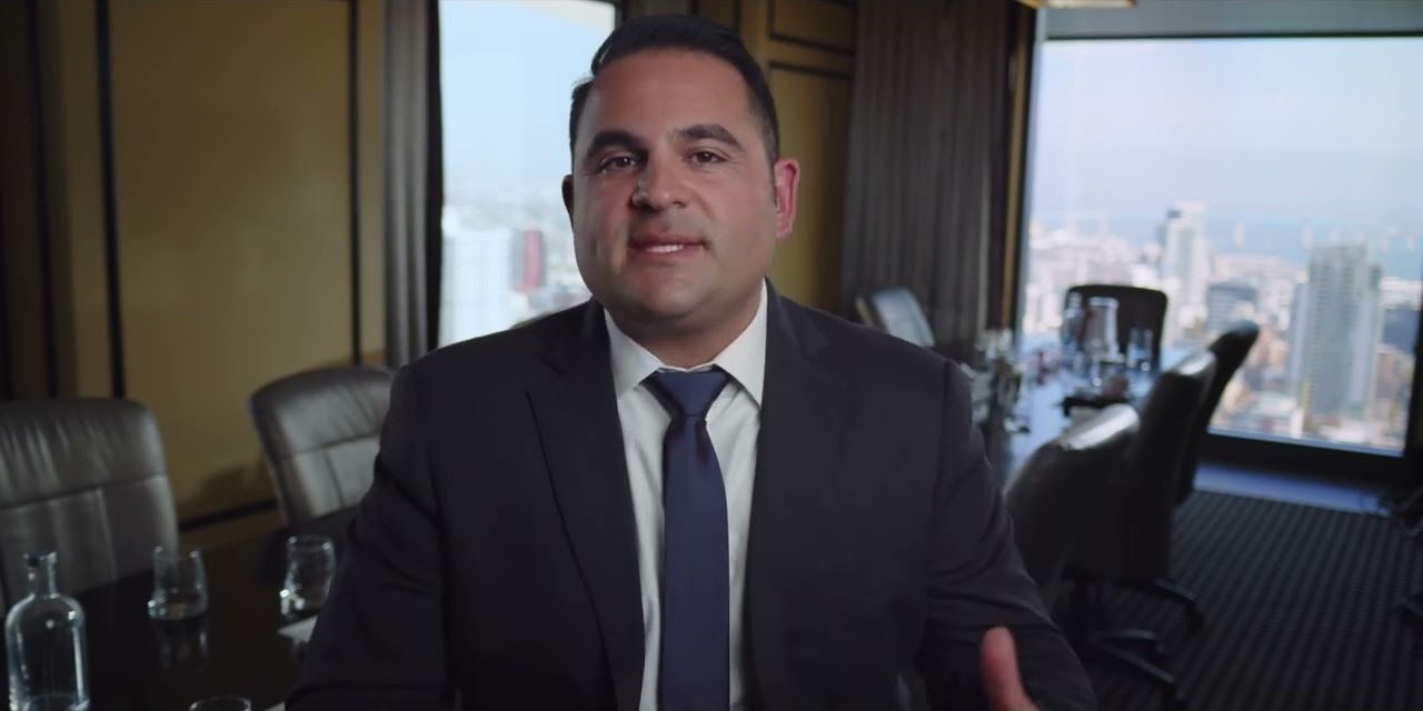 An attorney in a dark suit talking to camera in a high-rise conference room