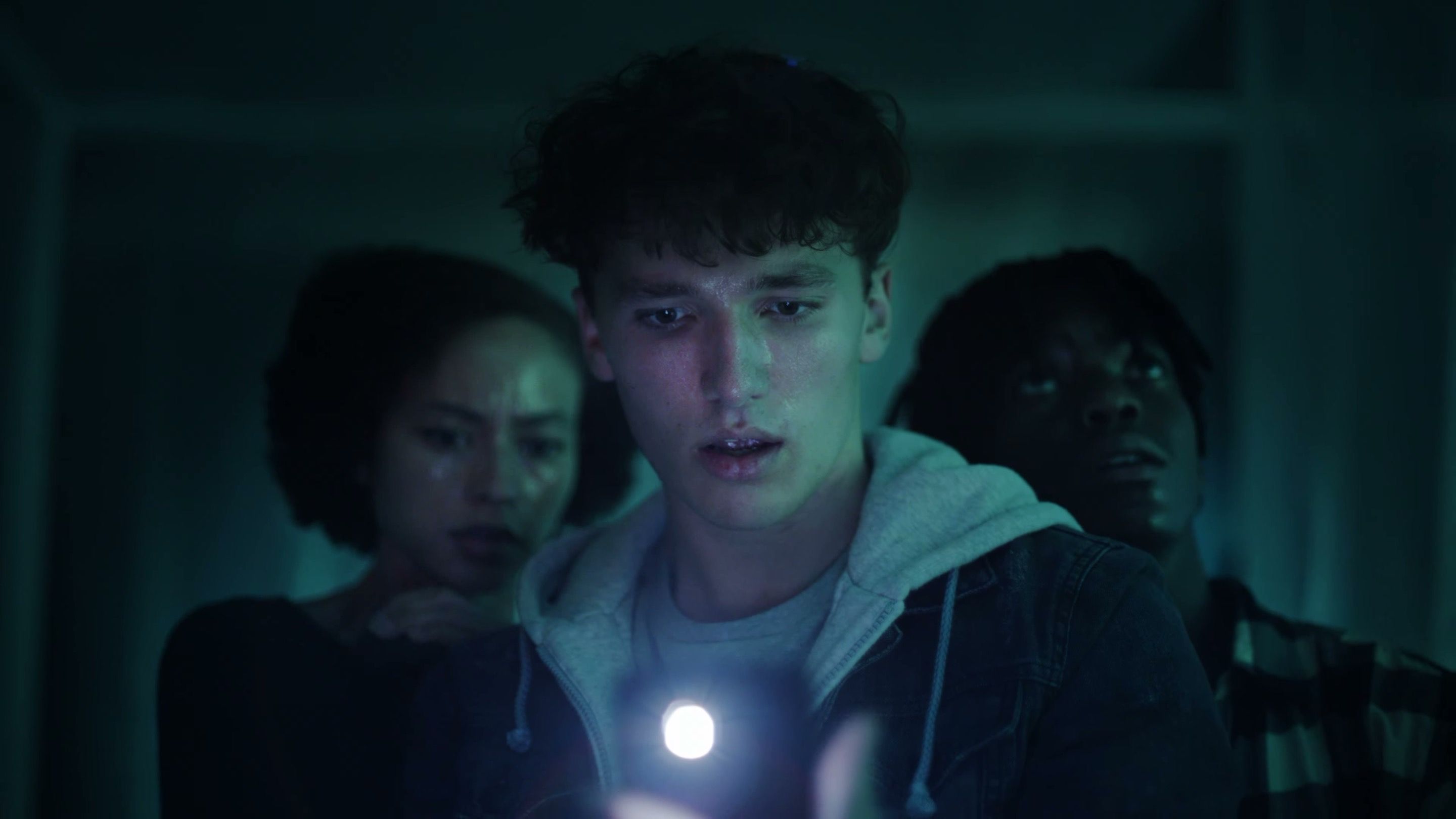 Three teenagers huddle in a dark hallway, lit by a flashlight, in the FDA youth vaping prevention trailer.
