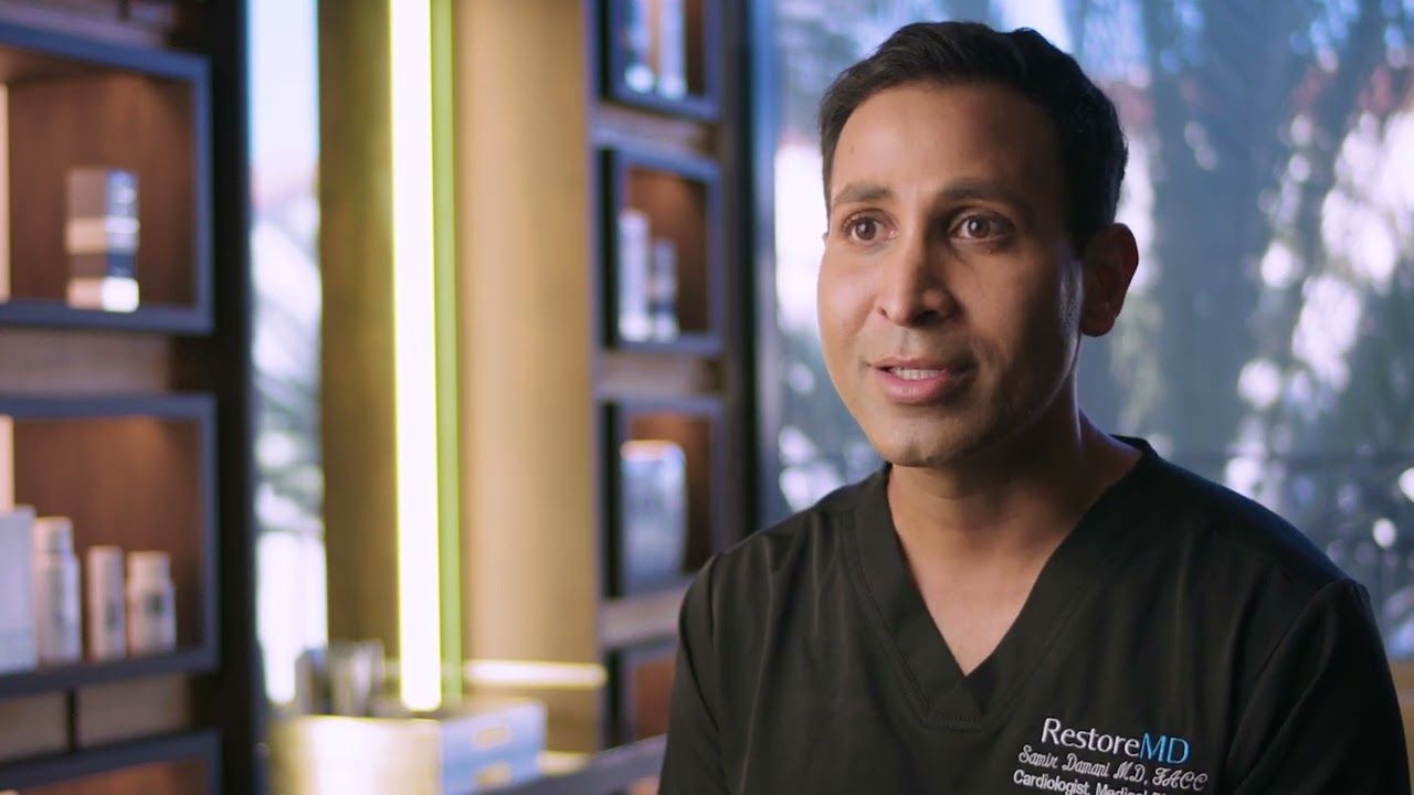 Dr. Samir Damani in RestoreMD scrubs explaining a topic in a softly lit clinic
