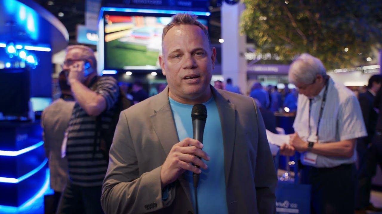 A presenter with a microphone on the trade show floor in front of the Chyron booth