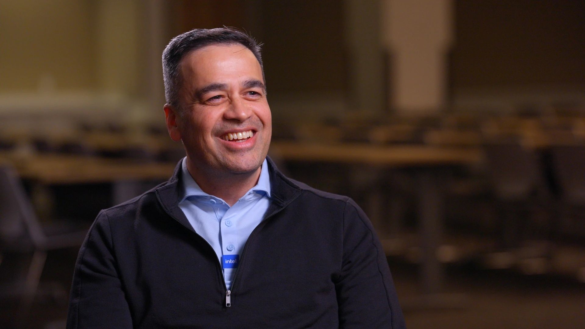 A smiling man wearing an Intel badge, interviewed in a warmly lit room
