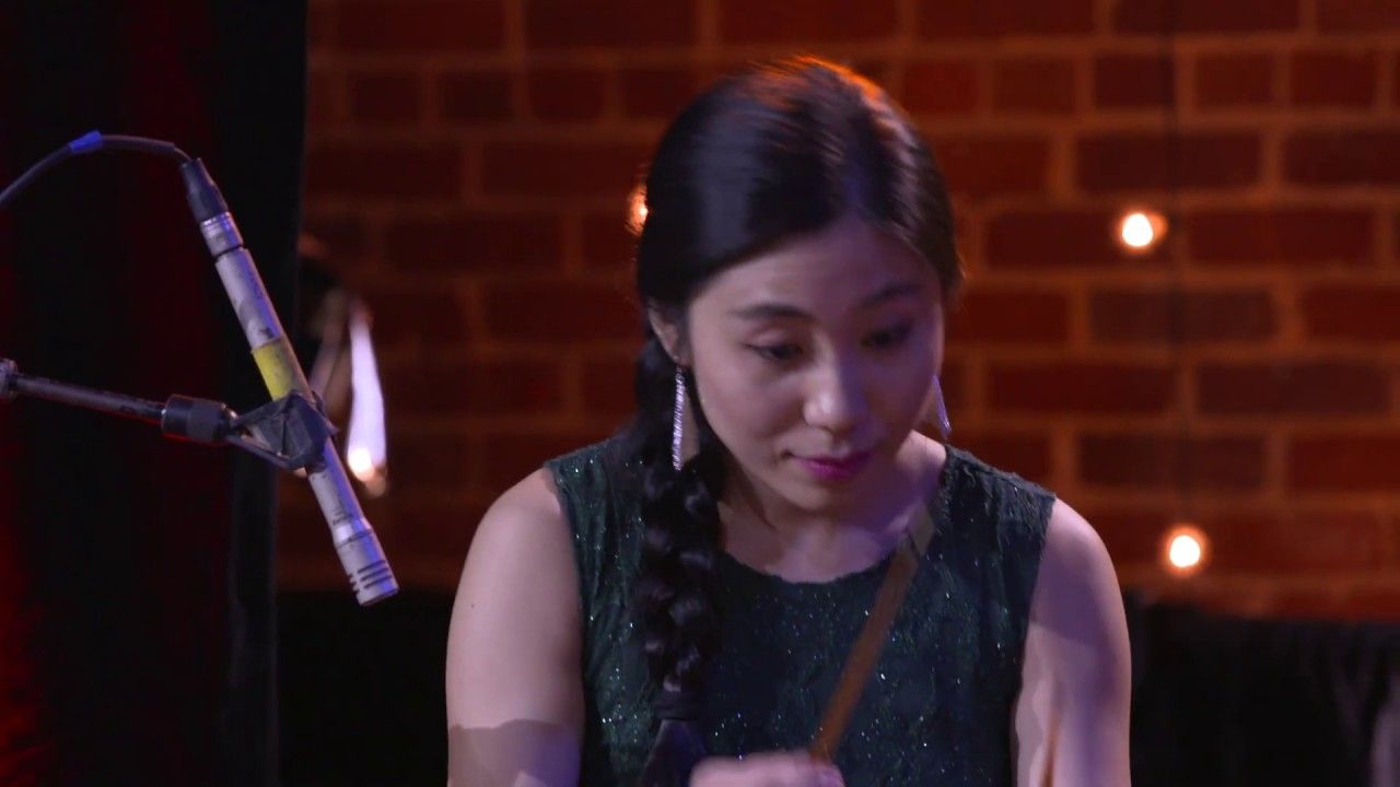 A violinist performs on the TEDxTysons stage in front of a brick wall strung with lights.