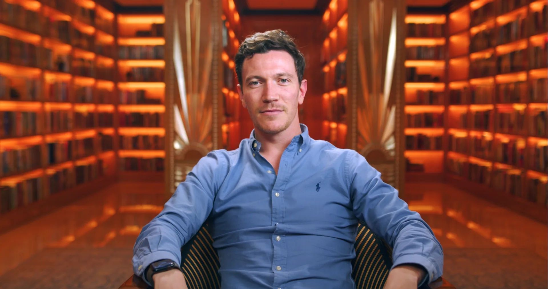 David Perell seated in a lamplit private library with warm curtains behind him.