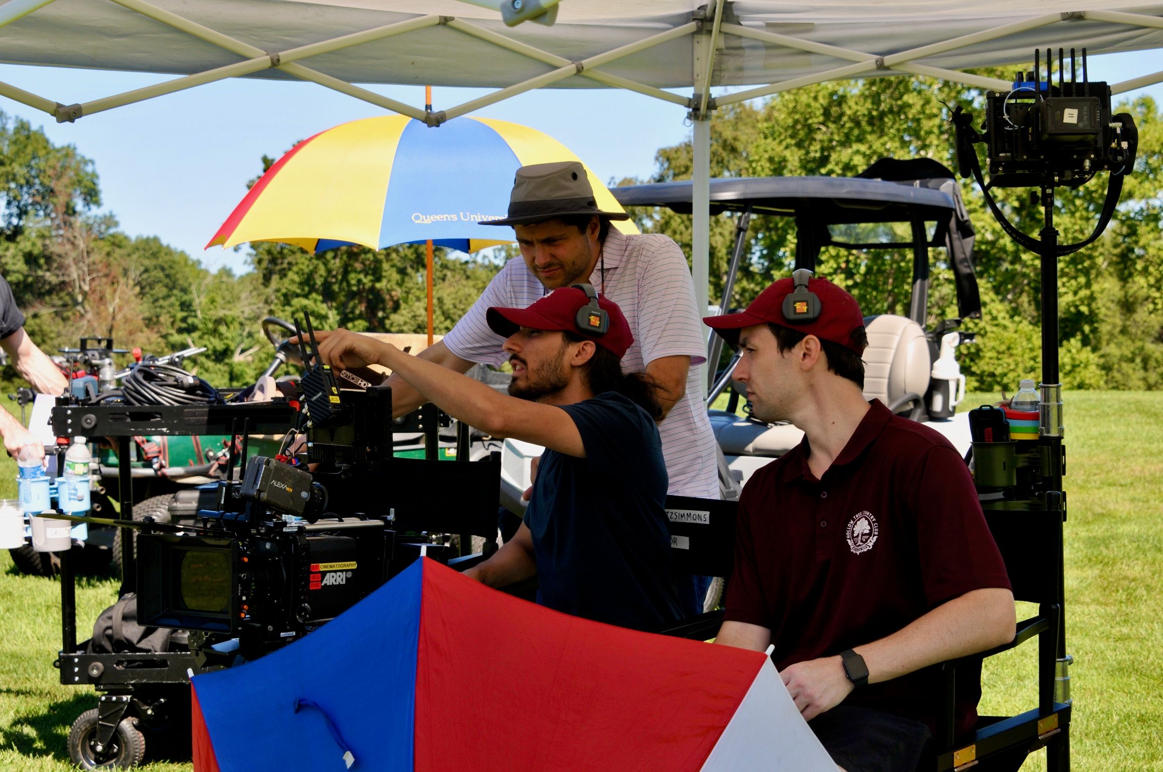Maui, in a red cap and headphones, points at the ARRI camera’s monitor beside a director and an assistant on an outdoor set.