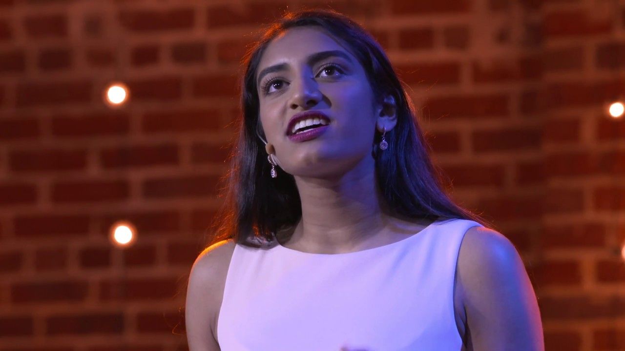 Marissa Sumathipala speaking on the TEDxTysons stage in front of a lit brick wall