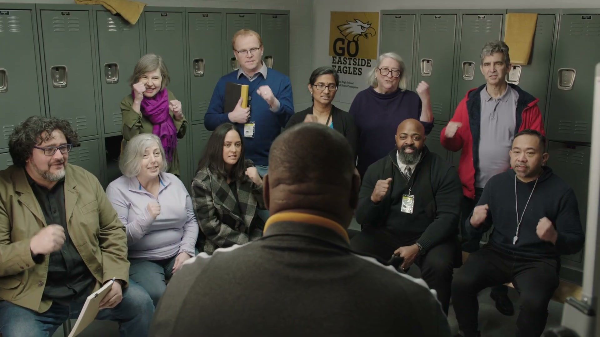 Teachers and parents cheer in a school locker room during the Selective Service “Coach” spot.