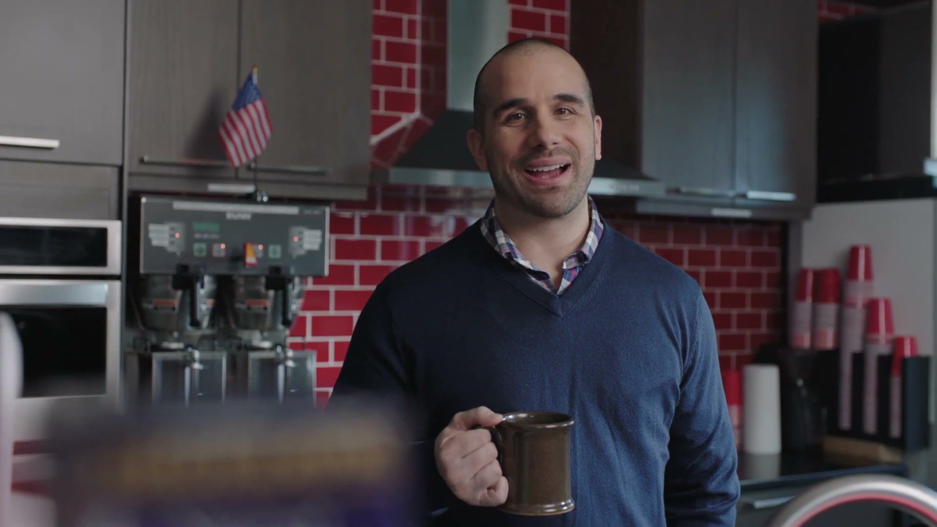 A smiling man holds a mug of coffee in a break room, from the Selective Service “Testimonials” spot.