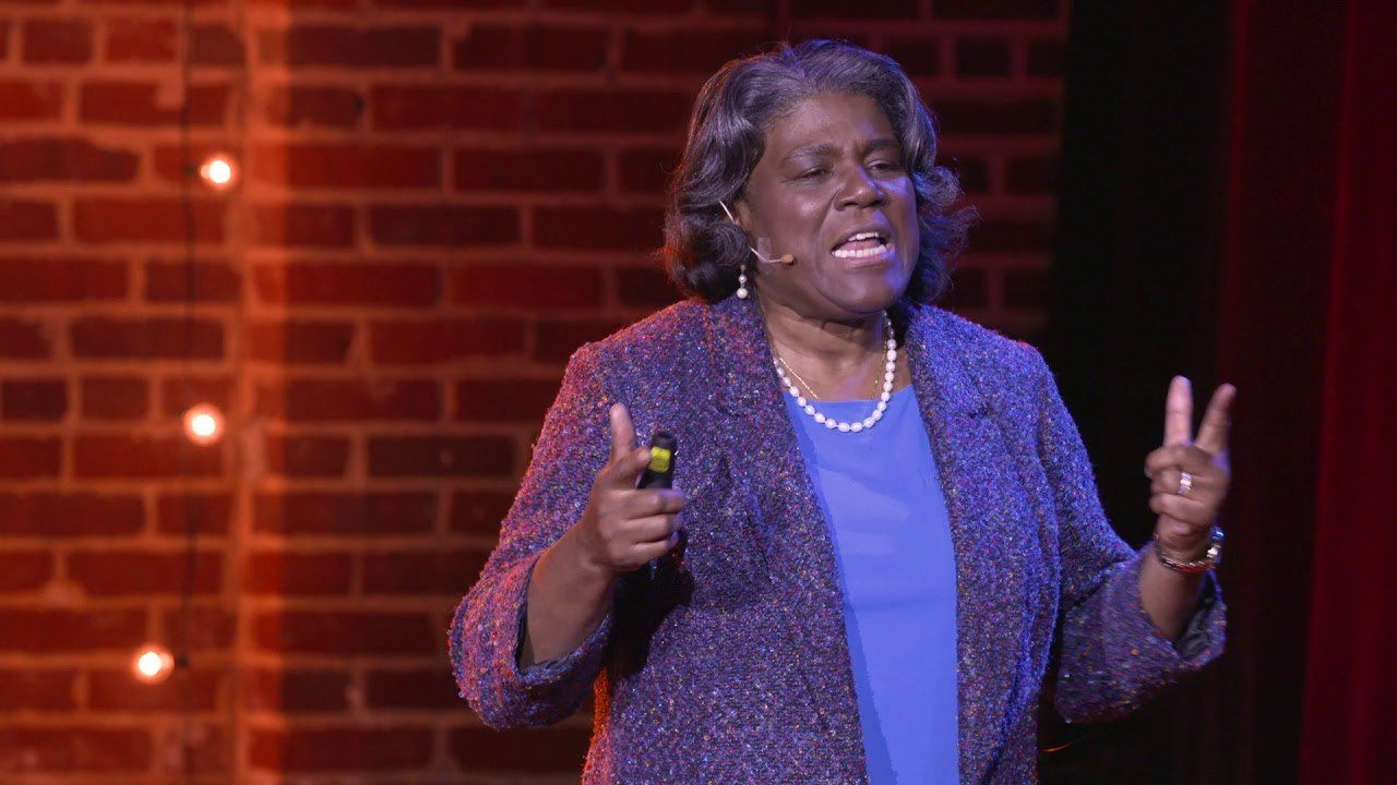 Linda Thomas-Greenfield speaks on the TEDxTysons stage in front of a red brick wall.