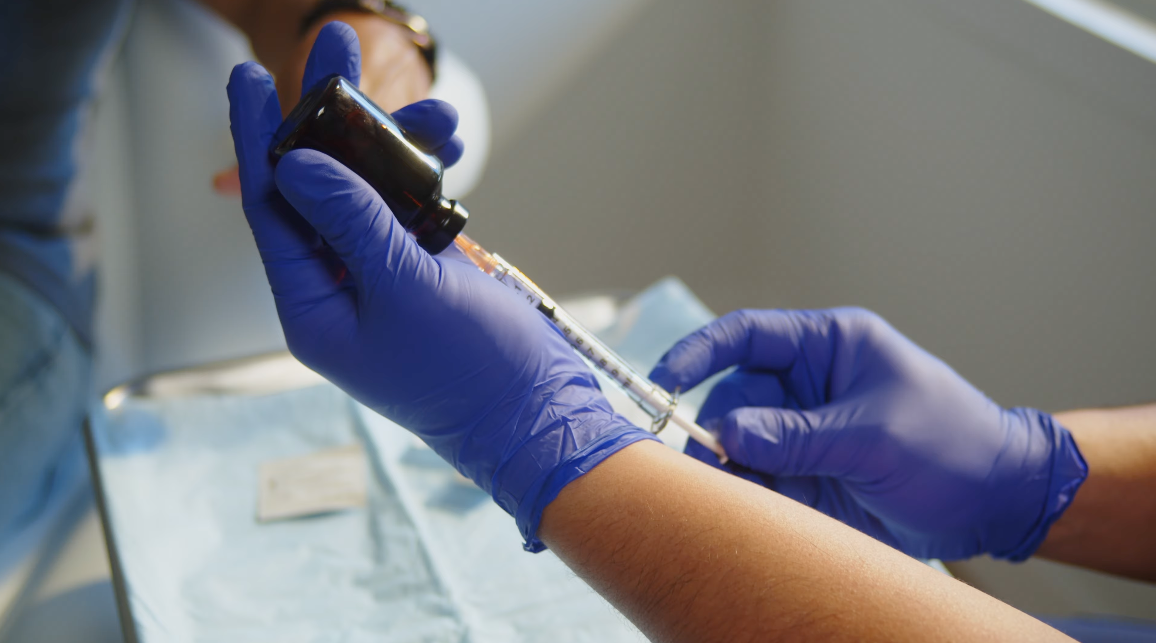 Gloved hands give an injection into a patient’s arm, from a clinical training film.