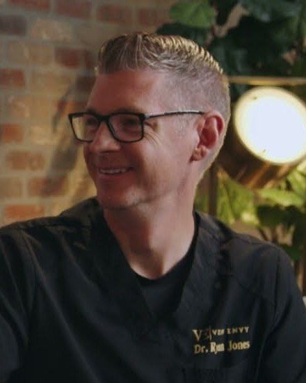 Dr. Ryan Jones of Vein Envy, in glasses and black scrubs, smiles during an interview.