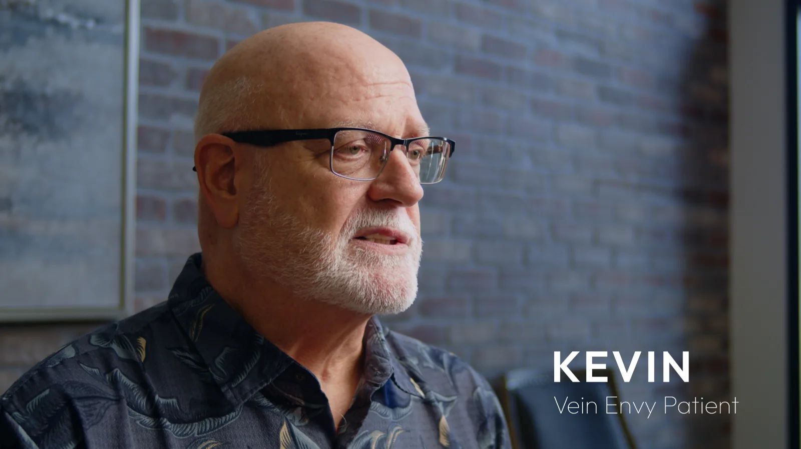 Kevin, a Vein Envy patient with glasses and a white beard, tells his story on camera in front of a brick wall.