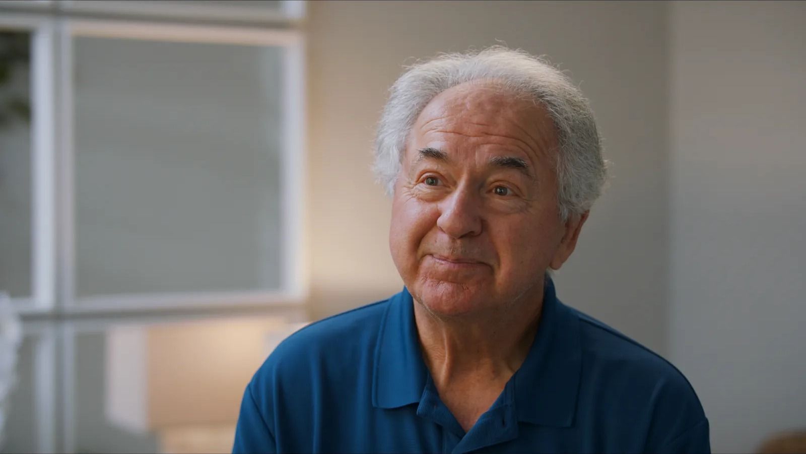 Wayne, an iThriveMD patient with white hair and a navy polo shirt, talks in a bright room.