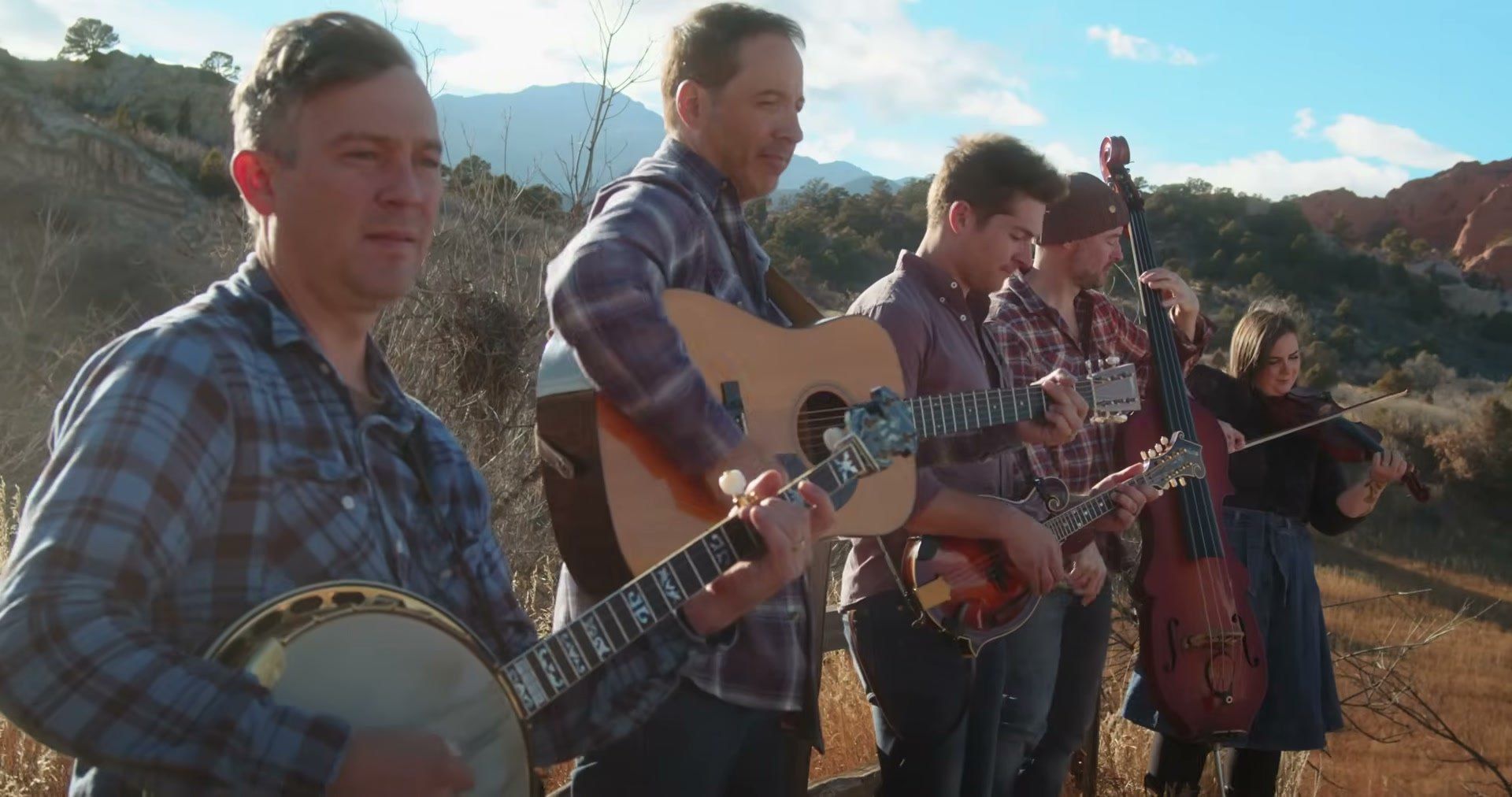 Yonder Mountain String Band plays banjo, guitar, mandolin, bass and fiddle in a dry field under a blue sky.